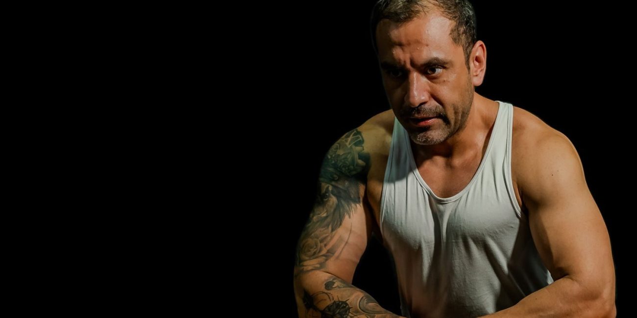 Muscular man with tattoos resting after an intense workout, showcasing determination and strength.