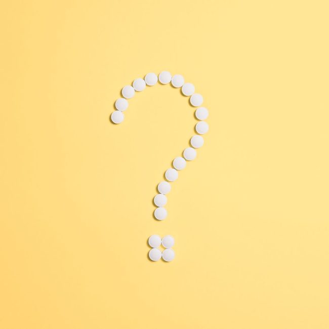 White pills arranged into a question mark shape on a vibrant yellow background.