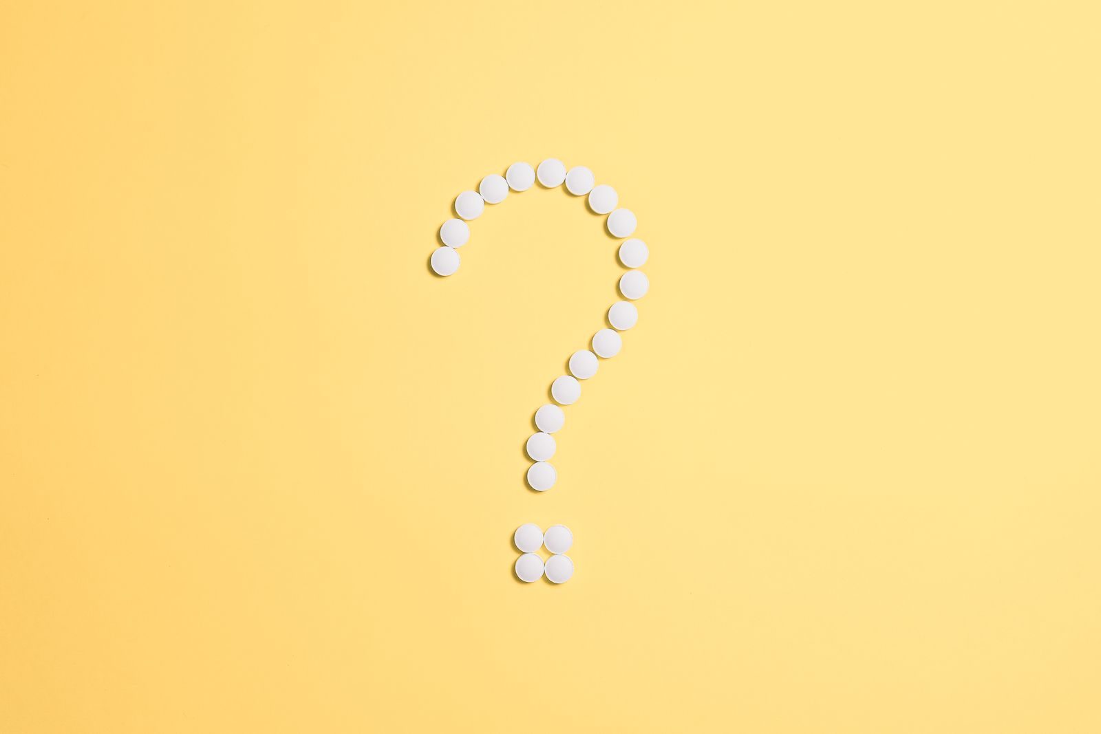 White pills arranged into a question mark shape on a vibrant yellow background.