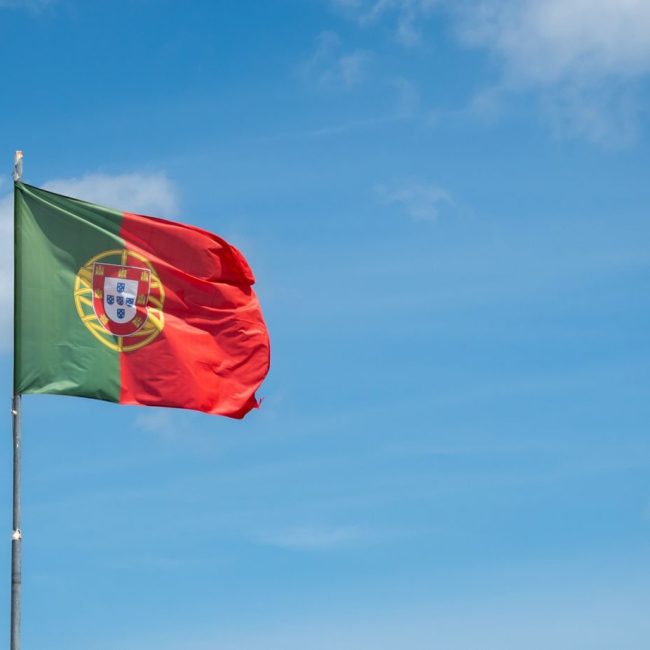 Vibrant Portuguese national flag gracefully waving against a clear blue sky in Cascais, Portugal.