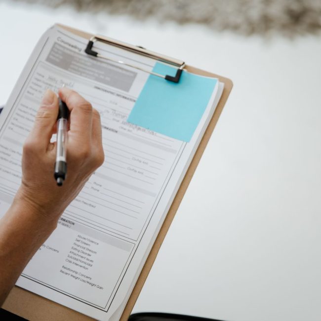 A person writes on a document using a clipboard indoors.