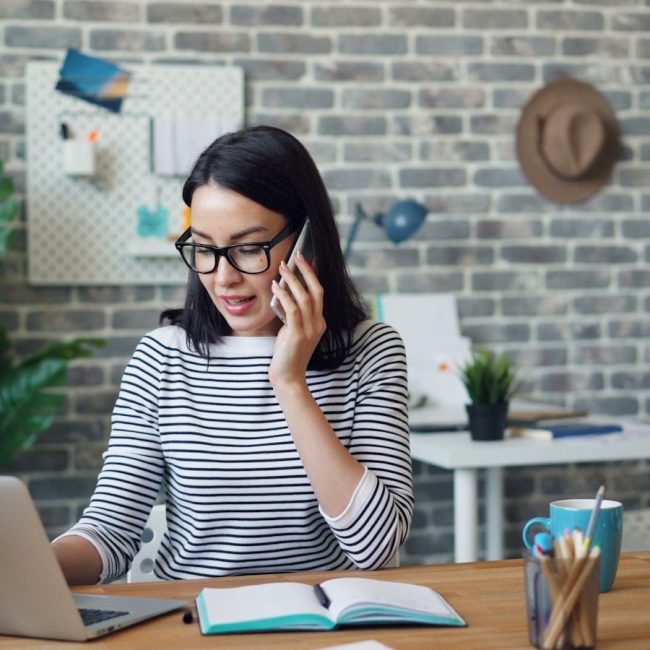 a woman talking on a cell phone while using a laptop