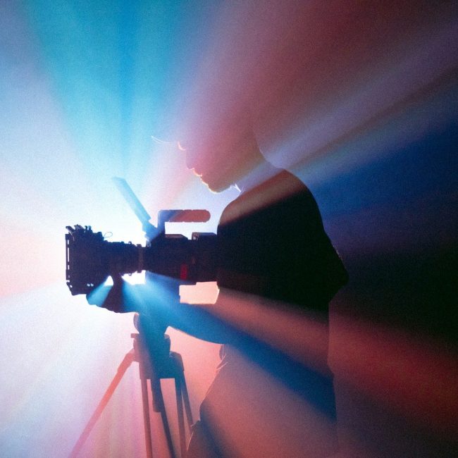 A person filming with a camera on a tripod in blue and red light