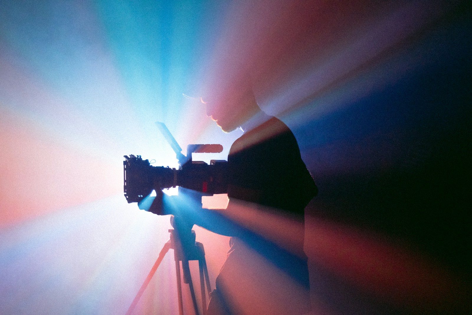 A person filming with a camera on a tripod in blue and red light